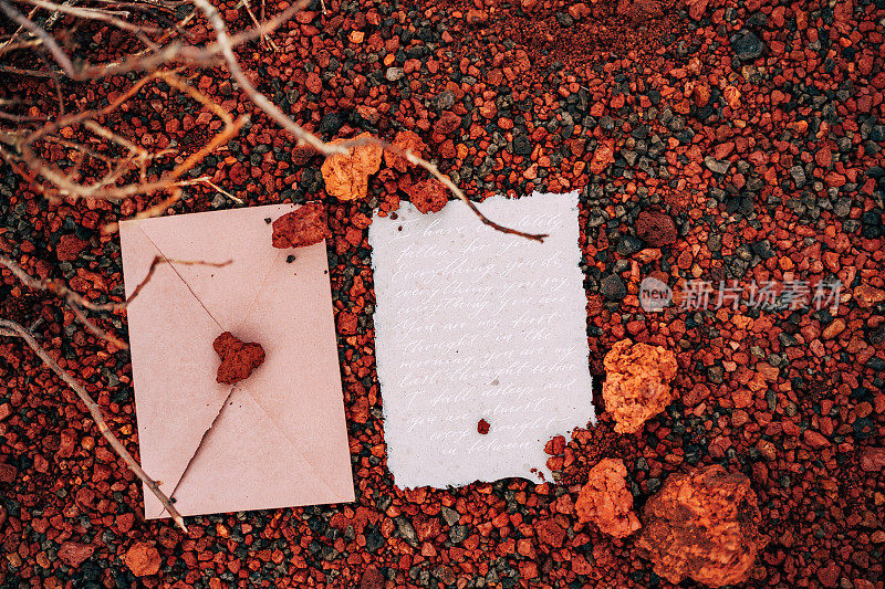 在红色的石头和枯枝的背景下，放着封好的信封和一封填满的请柬