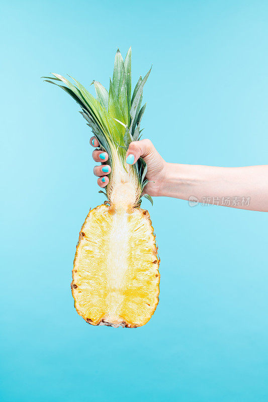 手持鲜菠萝切成两半，背景为亮蓝色。
