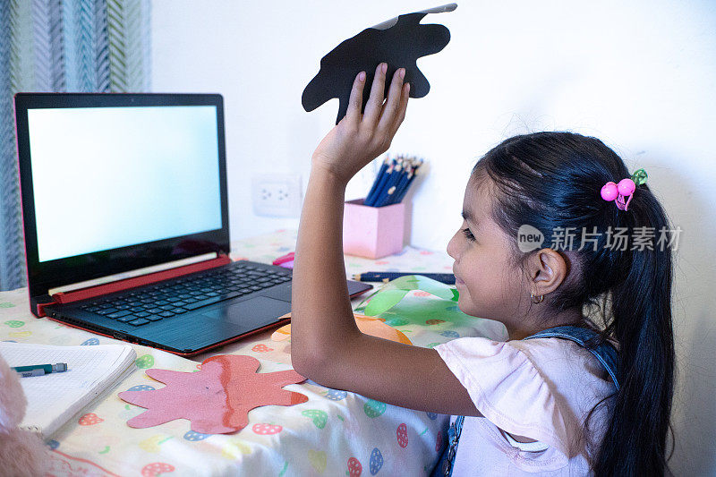 一个小女孩在家里用笔记本电脑facetime视频通话，使用在线虚拟课堂缩放，社交距离