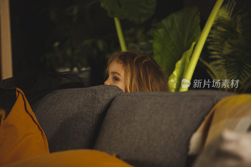小女孩躲在沙发后面，玩捉迷藏