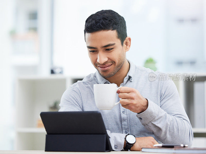 一个年轻的商人一边喝咖啡一边用他的平板电脑