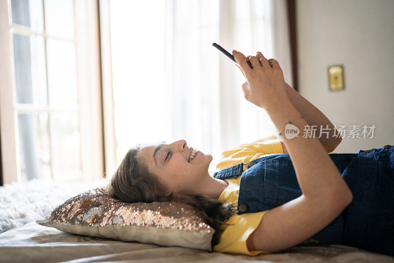 一个快乐的少女躺在床上，在家里用智能手机发短信