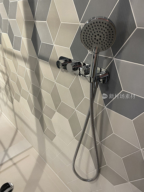 现代浴室的特写图像，独立的淋浴间，灰色，黑白几何墙砖的立方体图案设计，当代铬淋浴挂在墙上，排水孔