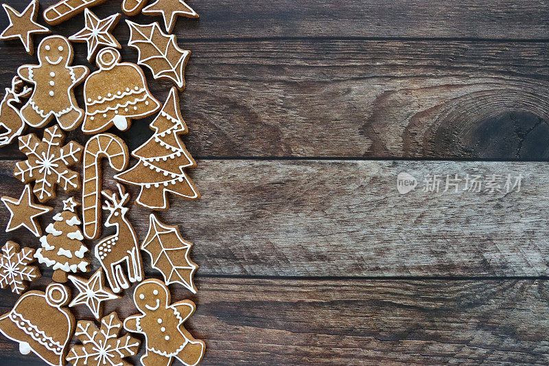 节日形象设计的圣诞海报框，自制的立柱，剪出形状的姜饼圣诞树，拐杖糖，铃铛，冬青树叶，雪花，驯鹿，星星和姜饼人饼干上的蓝色，木纹背景，复制空间