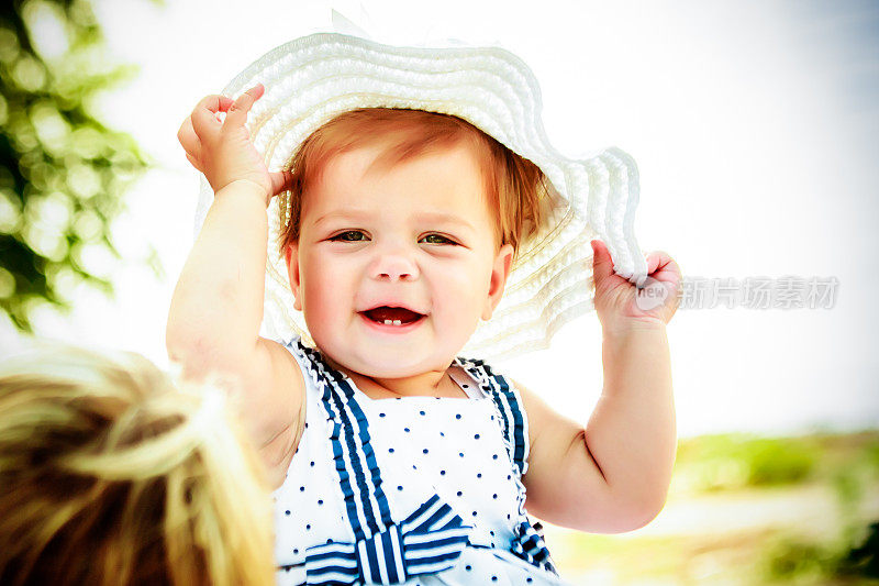 戴着白色大帽子的小女孩。婴儿的眼泪从帽子。美丽的小女孩在海滩上。