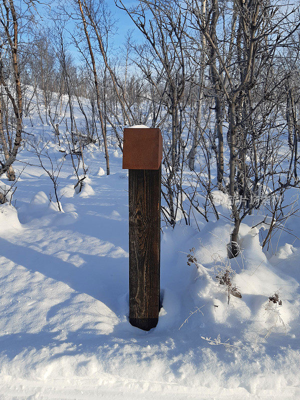 雪域拉普兰景观中的木桩。蓝色天空下的极地圈上有雪的徒步旅行路标。北欧国家的性质。