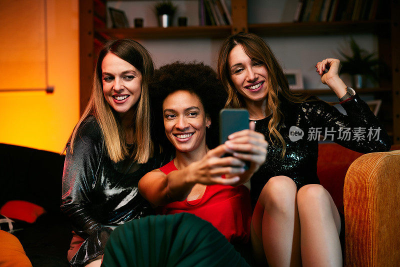 晚上的家庭聚会上，三位多元文化的女性朋友坐在客厅里自拍。