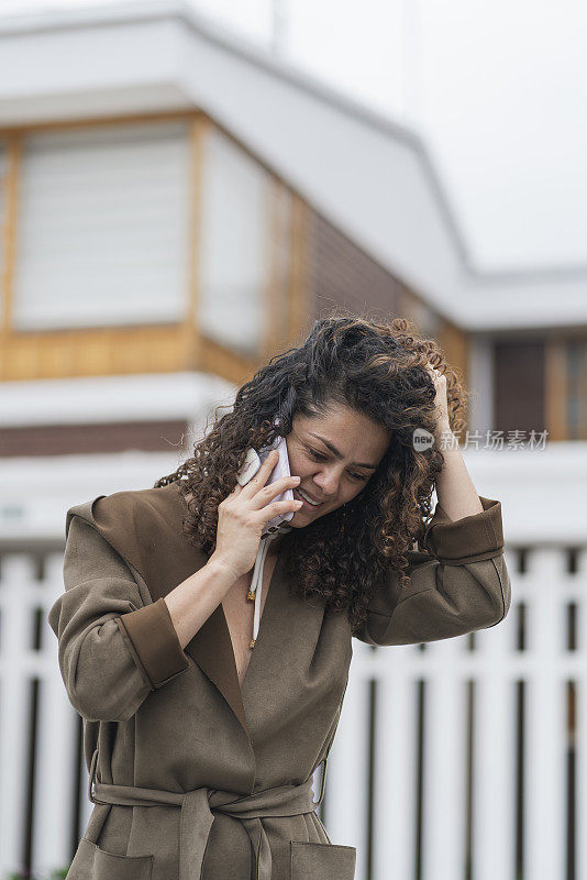 一头卷发的拉丁女子正在屋外用手机打电话