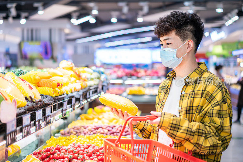 年轻英俊的亚洲男子戴着防护口罩，在超市买水果