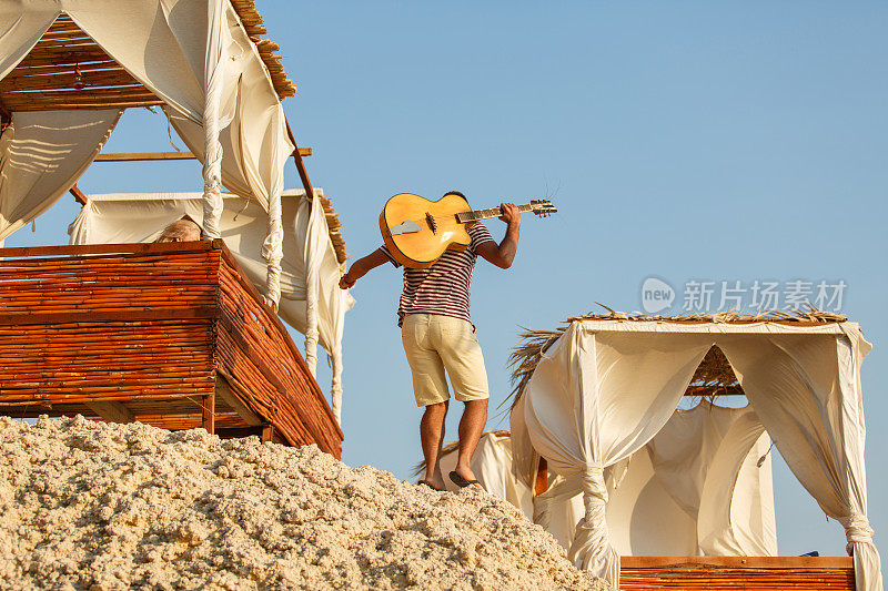 偷拍到一个年轻人走在海滩上，肩上背着一把原声吉他