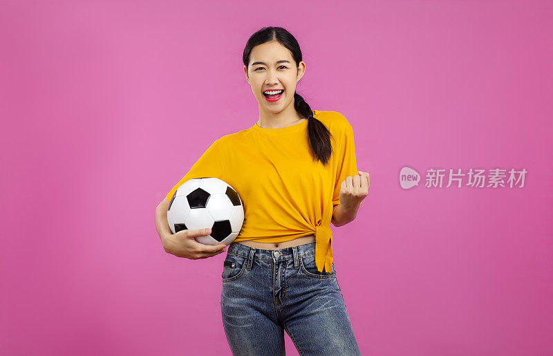 开朗的亚洲年轻女子在孤立的粉红色背景下拿着一个足球，国际足联世界杯的概念