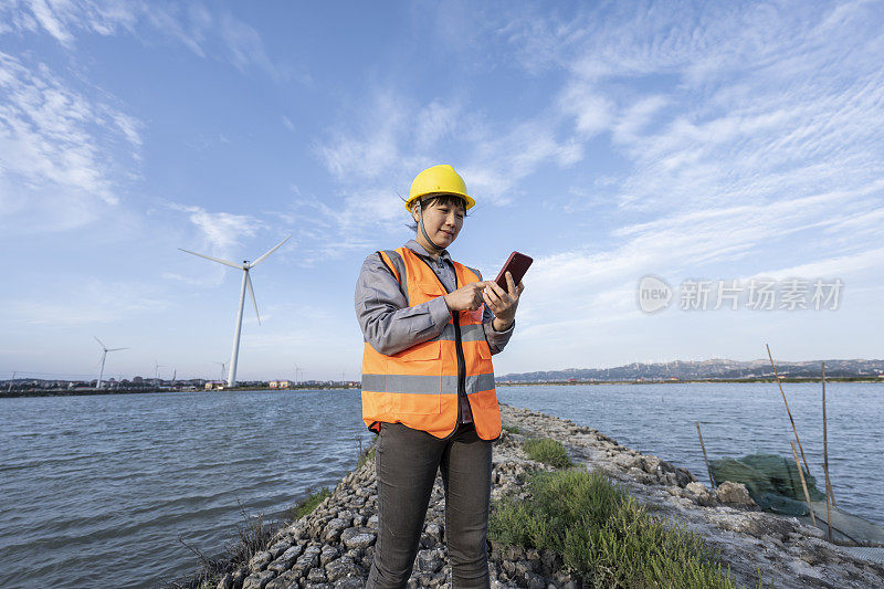 一位女工程师在海边的风力发电场使用手机。