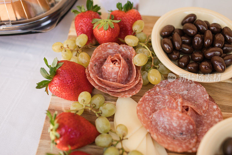 鸡尾酒时间熟食板充满了萨拉米玫瑰，切片奶酪，绿葡萄，红草莓，黑橄榄，黑巧克力覆盖杏仁在南佛罗里达的户外活动