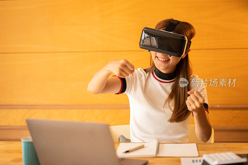 在家里戴着VR眼镜的开朗的白人女性。年轻女子享受眼镜与想象的手做想象的手势在虚拟现实设备在桌子上的笔记本电脑和计算器文件。