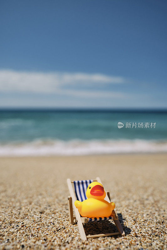6月一个阳光明媚的日子，康沃尔郡的佩登·温德海滩上，一只橡皮鸭坐在沙滩假日的躺椅上。