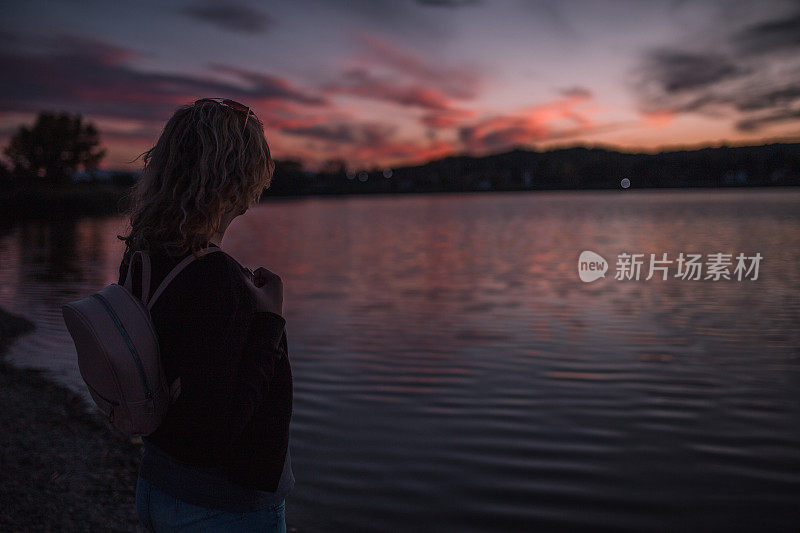 一个女人享受她的假期在湖上看日落的背影
