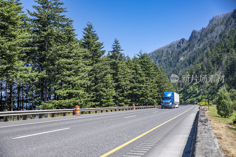 时髦的蓝色大卡车在运输货物的干货车半挂车运行在转弯宽阔的公路在哥伦比亚河峡谷