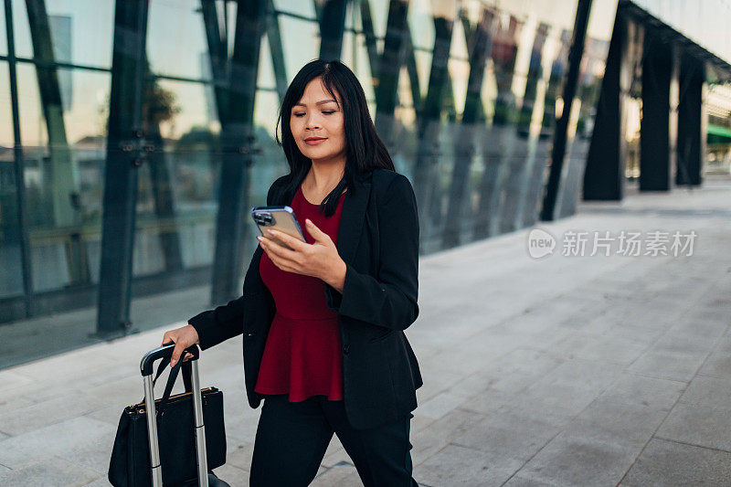 一位女商人一边拿着行李箱一边用手机上网