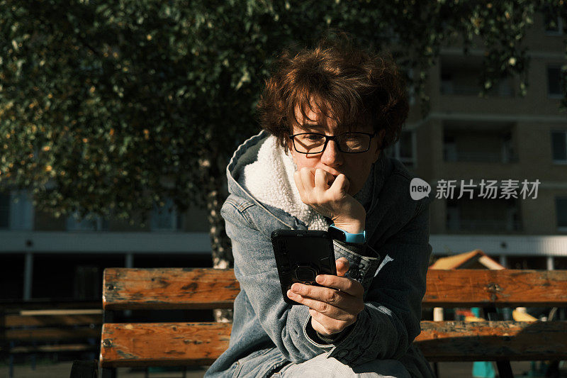 悲伤抑郁的女人正坐在长凳上用手机