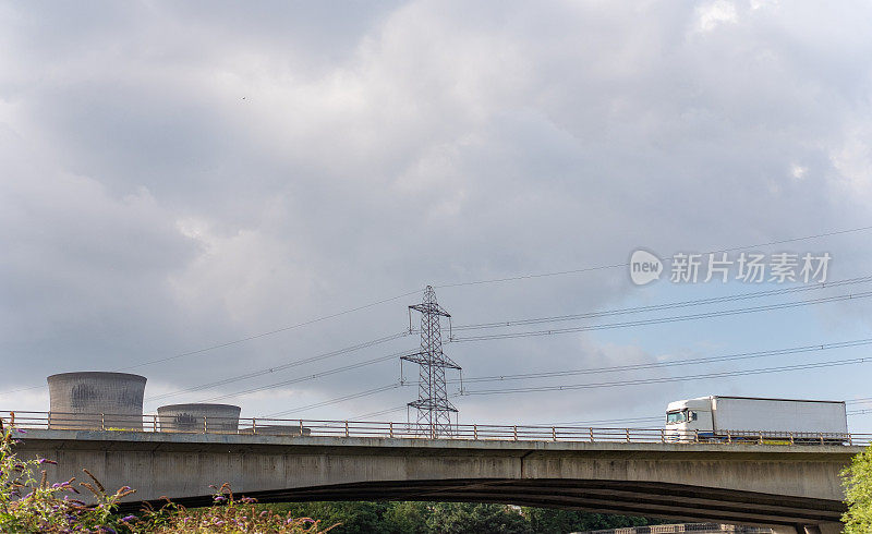 货物运输铰接式卡车行驶在高速公路河桥上，桥上有发电厂和电线的工业背景。用Lensbaby相机拍摄故意模糊