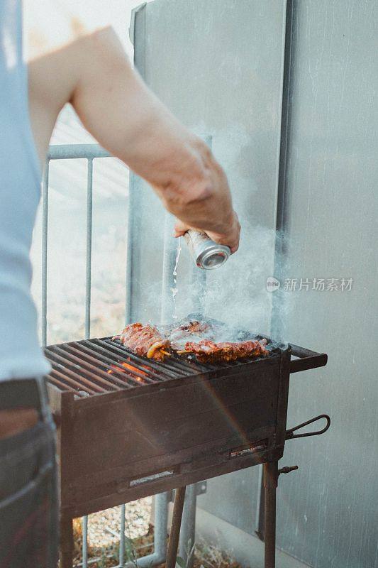 垂直拍摄一只手把一罐水倒在烤肉架上的肉上