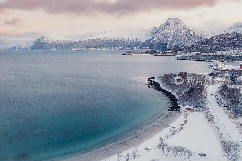 航拍图像的女人和男人走在风景秀丽的turqouse海滩在雪与山景在挪威