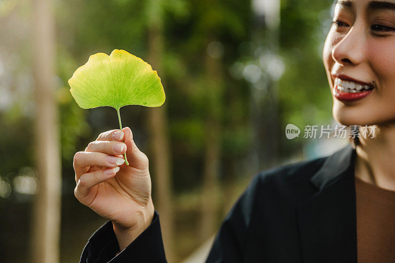 一个迷人的女人站在城市的街道上，手里拿着一片银杏叶。