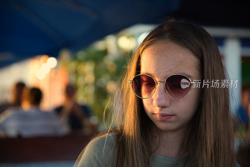 一个十几岁的女孩坐在日落时分的夏日户外餐厅的肖像