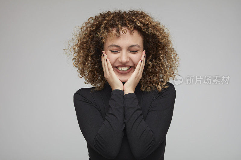 年轻的卷发女子把手放在脸颊上，摆出幸福的姿势。