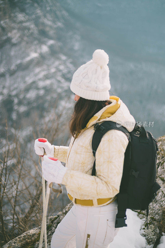 年轻女子背着背包，在美丽的雪山中拄着登山杖散步