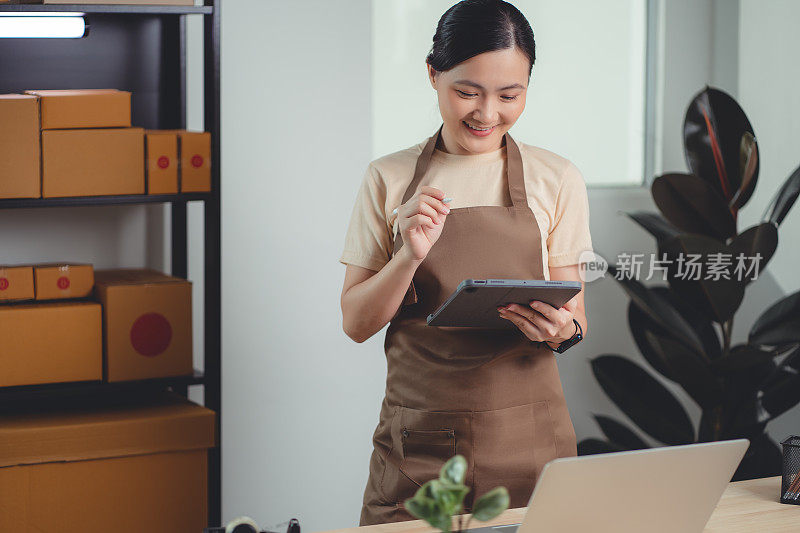 亚洲女性在线卖家使用平板电脑在家庭办公室检查产品库存。