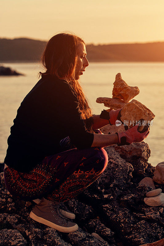 一个女人的剪影平衡岩石和石头在海洋海岸在日落日出时间。