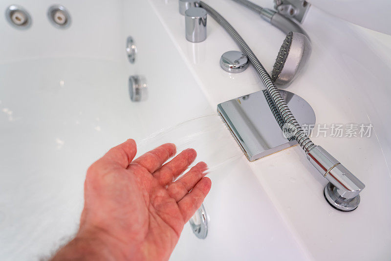 水从按摩浴缸的龙头流出，男人的手用手指触摸水。