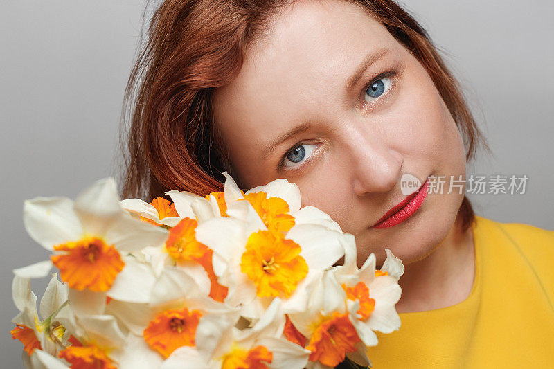 中年妇女的肖像，穿着黄色上衣，拿着一束水仙花，看着镜头