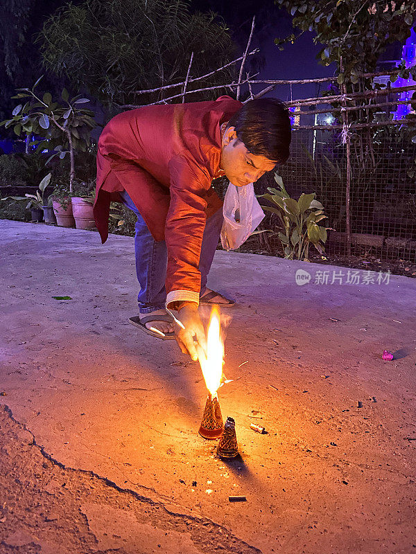 印度男子身穿库尔塔传统服装，手持点燃的朋克(闷烧棍)，弯腰点燃喷泉烟花，印度传统节日的灯光，排灯节庆祝活动