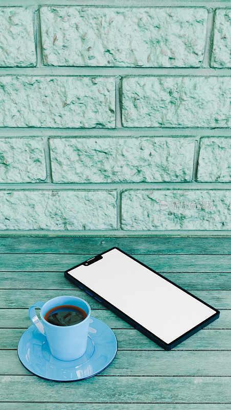 一杯咖啡和手机放在靠近砖墙的蓝色木桌上，放松和科技的主题