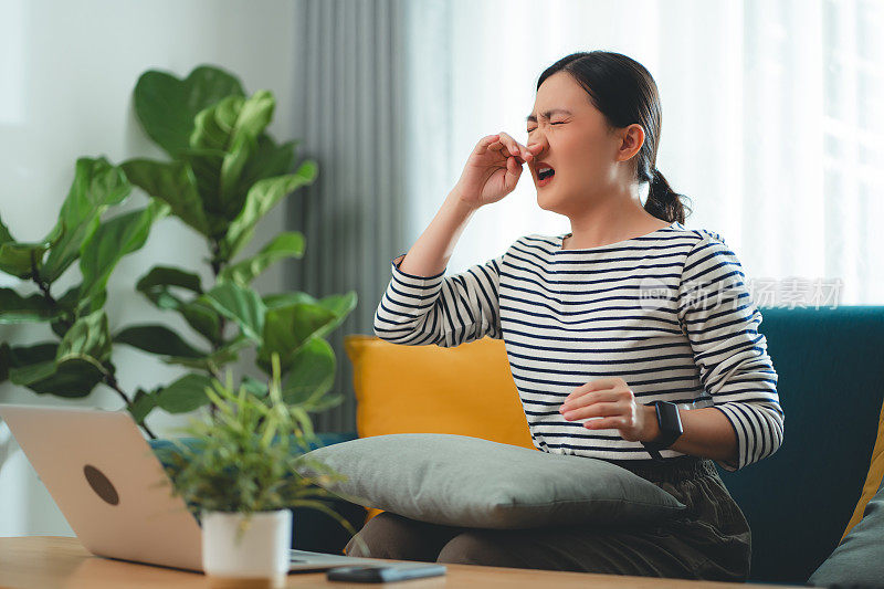 一名亚洲妇女因发烧、流鼻水、咳嗽及打喷嚏，在家工作。