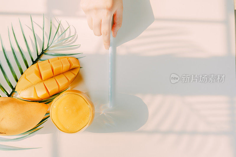 俯视图和平坦的夏日水果从美女手里拿着芒果汁，用叉子吃芒果片白色孤立的背景