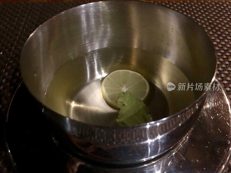 餐厅餐桌上的铜印度指碗配以柠檬片和温水，用餐者在吃完晚餐后为卫生洗手和手指拍照，豪华的红色和金色天鹅绒桌布