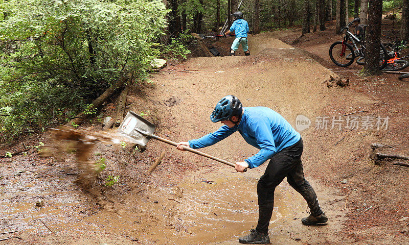 在雨林中，两名山地自行车手用铲子把自行车道上的水铲掉