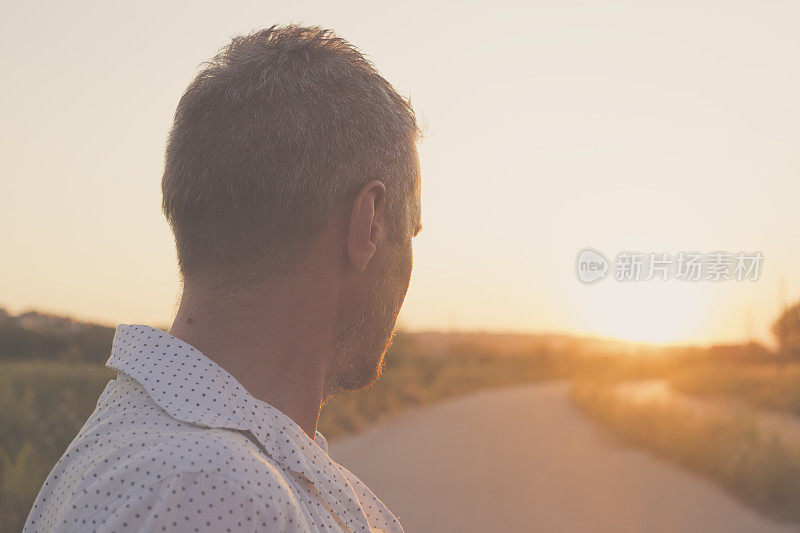 英俊的成年男子站在柏油路上，望着远处的夕阳