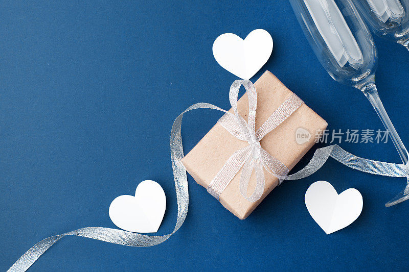 情人节贺卡。空酒杯酒纸折纸心在经典的蓝色背景。拷贝空间，简约二月浪漫概念，婚礼派对