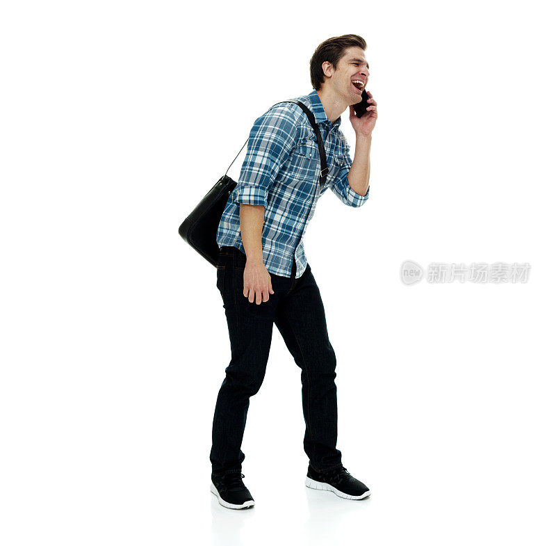 白人男性站在白色背景前，戴着邮差包，拿着包，使用手机