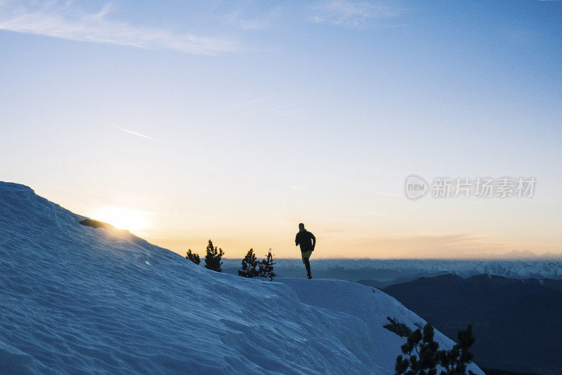 黎明时分，一名徒步运动员爬上雪山的山脊