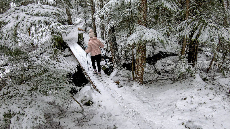 女性徒步旅行者走在被雪覆盖的木板路上