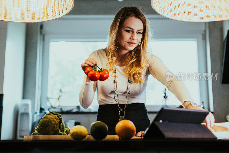 一个女人在做蔬菜餐，在平板电脑上阅读菜谱