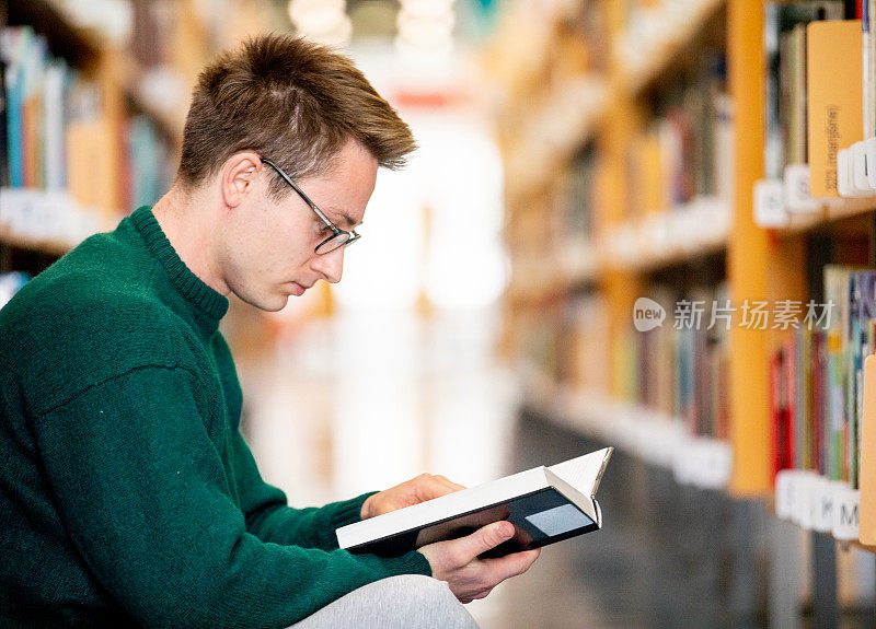 年轻的成年学生坐在图书馆地板上学习