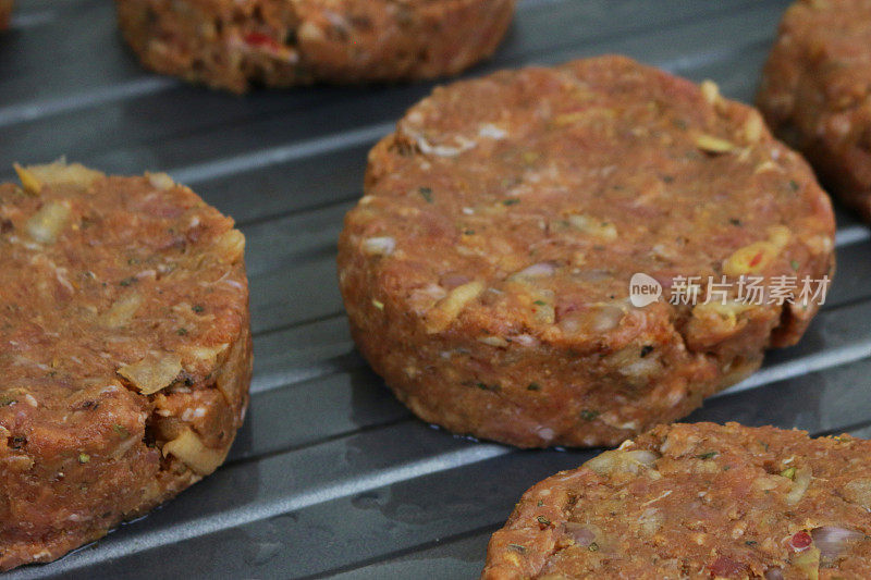 一排排的自制牛肉汉堡肉饼，在厨房的工作台上烤盘准备在烤箱中烹饪