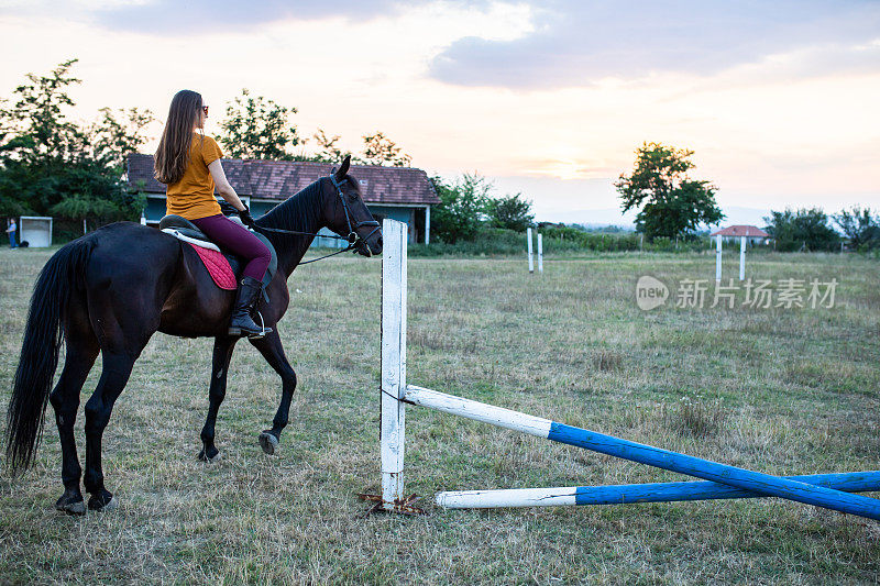一个年轻女子骑着马在旁边跳跃障碍