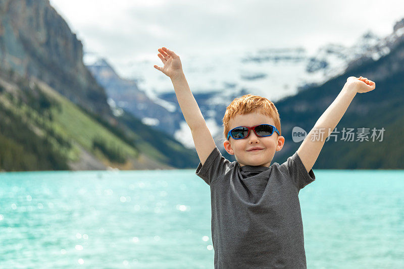 快乐的年轻可爱的红发男孩在夏天的路易斯湖举起手臂